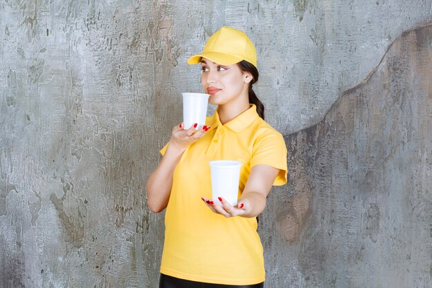 黄色い制服を着たセールスウーマンが2杯のプラスチック製の飲み物を持って、1杯を他の人に渡します。