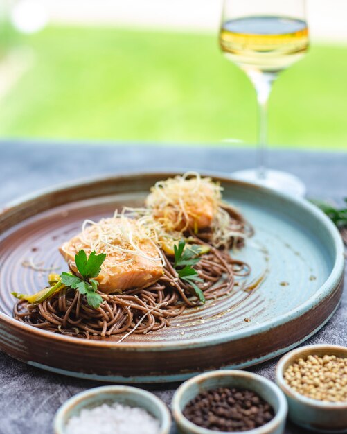 Salmon fillet garnished with sesame seed served with brown noodles and bell pepper