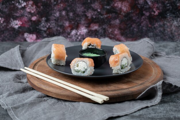 Salmon rolls in a black platter with wasabi sauce.