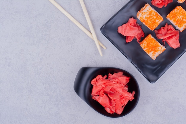 Salmon rolls and red marinated ginger in a black platter.