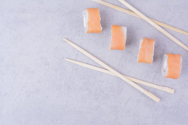 Salmon rolls and wooden chopsticks on grey.