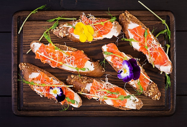 Salmon sandwiches with cream cheese and microgreen on wooden table. Canape with salmon.