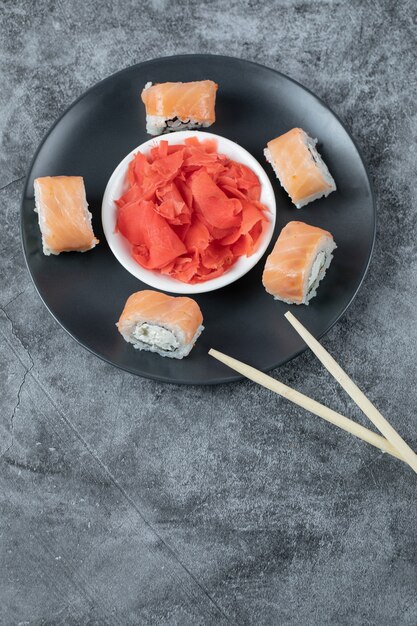 Salmon sushi rolls served with red ginger on a black plate.