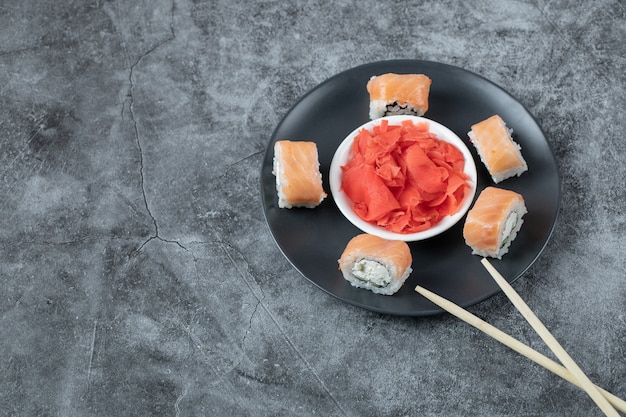 Free photo salmon sushi rolls served with red ginger on a black plate.