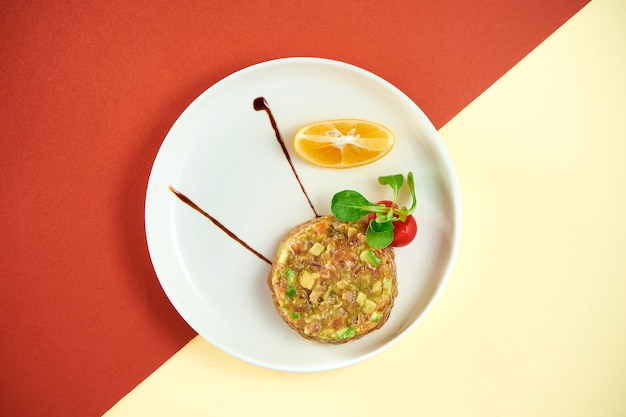 Тартар из лосося с авокадо и лимоном в белой тарелке на цветной поверхности. Premium Фотографии