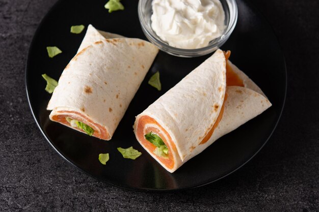 Salmon wrap sandwich roll with cheese and vegetables on black slate background