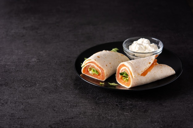 Salmon wrap sandwich roll with cheese and vegetables on black stone background