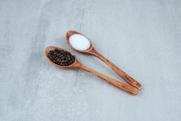 Salt and pepper grains on wooden spoons.
