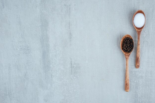 Salt and pepper grains on wooden spoons.