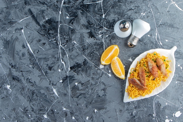 Salt, sliced lemon next to meat and noodle on a platter, on the marble background. 