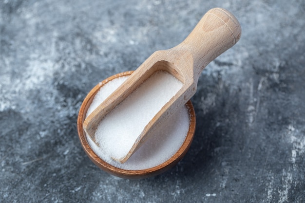 Salt in a wooden spoon on a marble background.