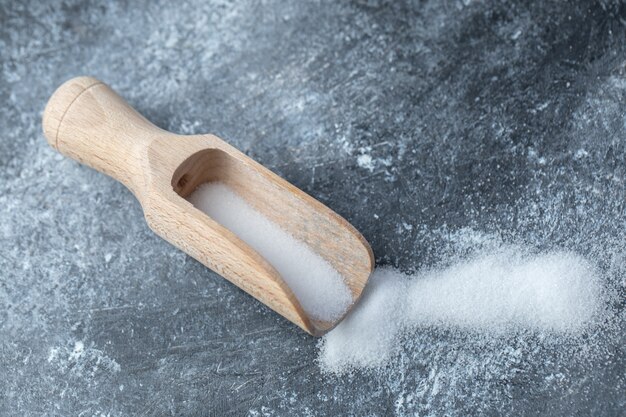 Salt in a wooden spoon on a marble background.