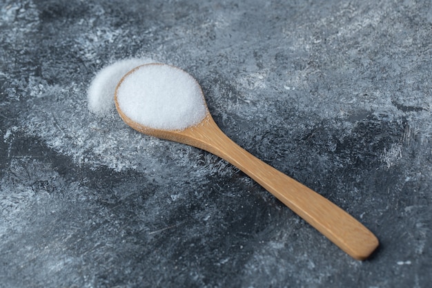 Salt in a wooden spoon on a marble background.