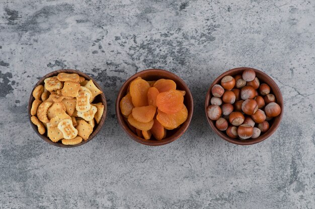 Salted crackers, dried apricots and hazelnuts in wooden bowls.