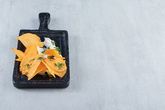 Salted crispy chips and fresh yoghurt on black cutting board.