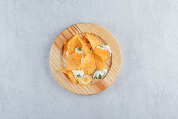 Salted crispy chips and fresh yoghurt on wooden plate.