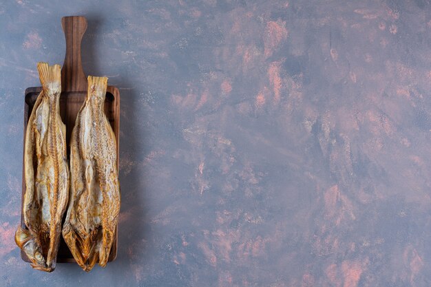 大理石の背景に、ボード上の塩漬けの魚。