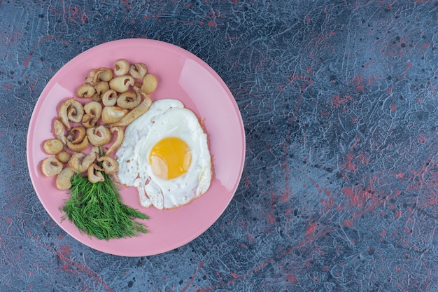 Uovo fritto salato e speziato con prezzemolo su un piatto rosa.