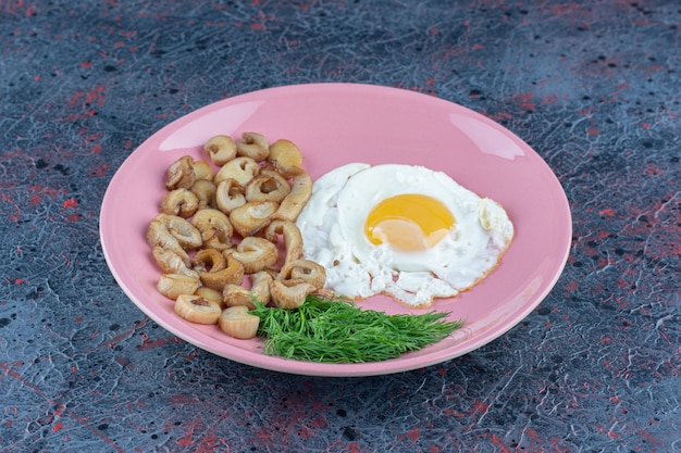 Salted and spiced fried egg with parsley on a pink plate 