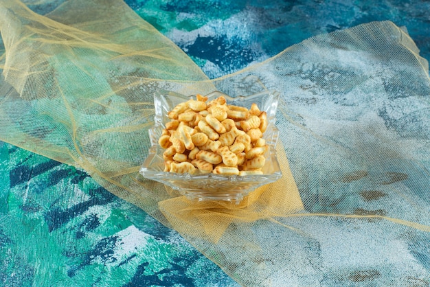 Salty fish crackers in glass bowl on tulle, on the marble table.