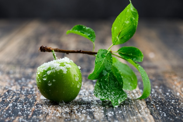 Salty green plum with branch side view on wooden and dark wall