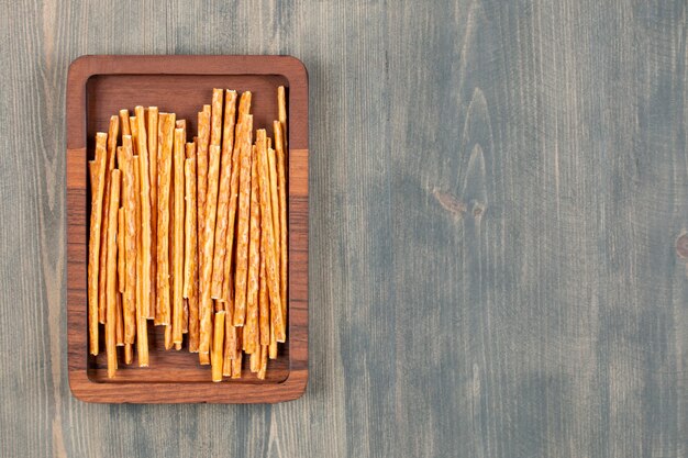 Salty pretzel sticks on wooden plate