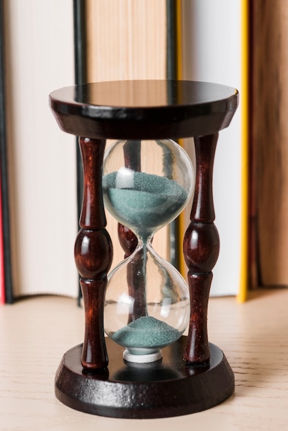 Sand falling in transparent hourglass on wooden desk
