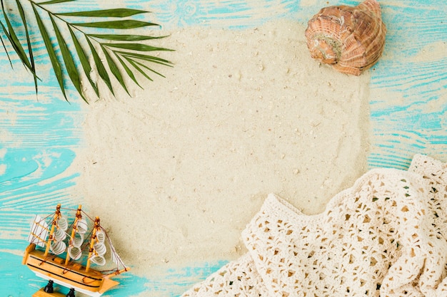 Sand among plant leaf near seashell and toy ship on board