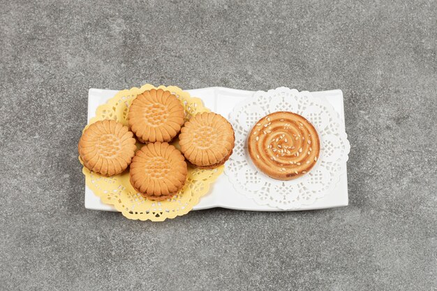 Sandwich cookies and biscuit with sesame seeds on white plate