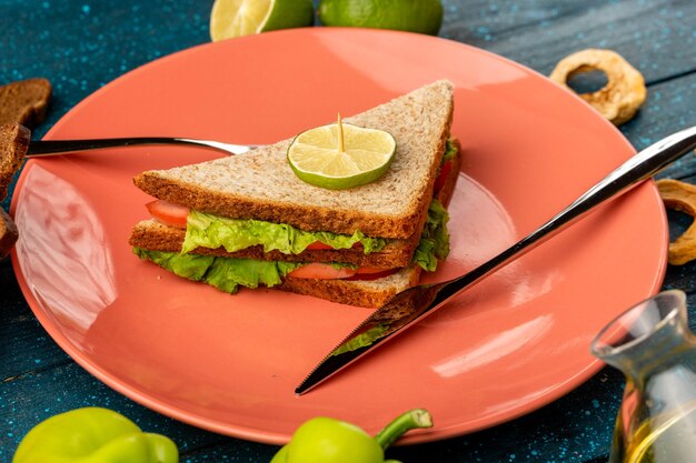 бутерброд внутри тарелки вместе с зеленым болгарским перцем и лимоном на синем