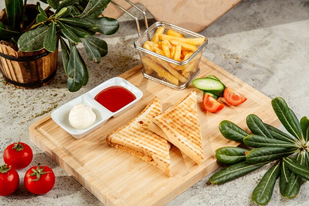 Sandwich served with french fries and sauce on a cutting board