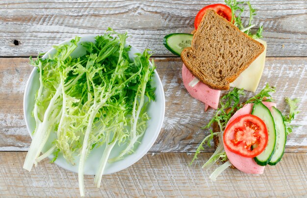 Sandwich with bread, cheese, tomato, cucumber, sausage, greens flat lay on a wooden table