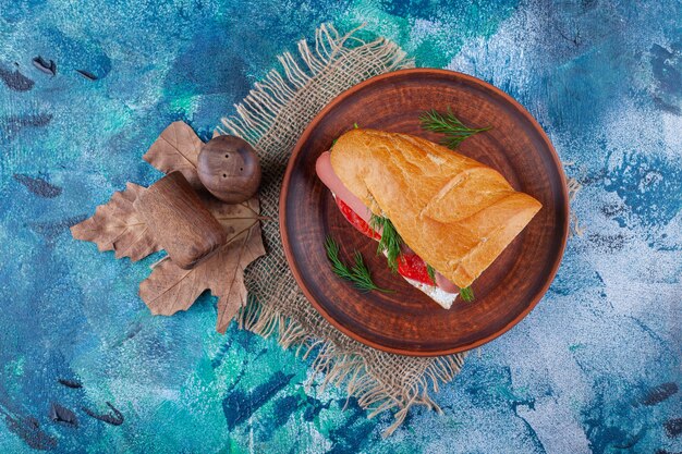 Сэндвич на деревянной тарелке на салфетке из мешковины на синем.
