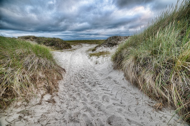 Sandy pathway surrounded by hill under the cloudy sky