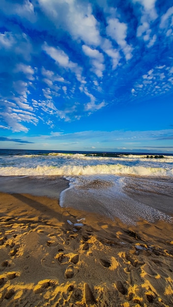 Sandy shore with foaming waves and a blue sky with clouds