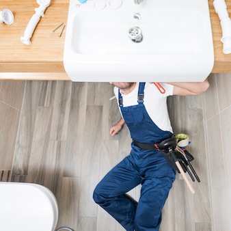 Sanitary technician lying under sink
