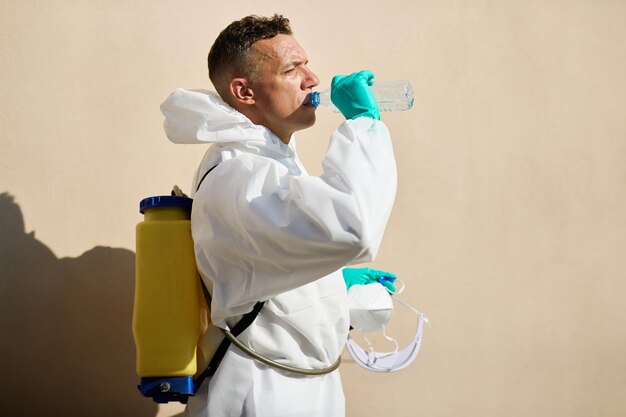 Sanitation worker in hazmat suit having a water break outdoors