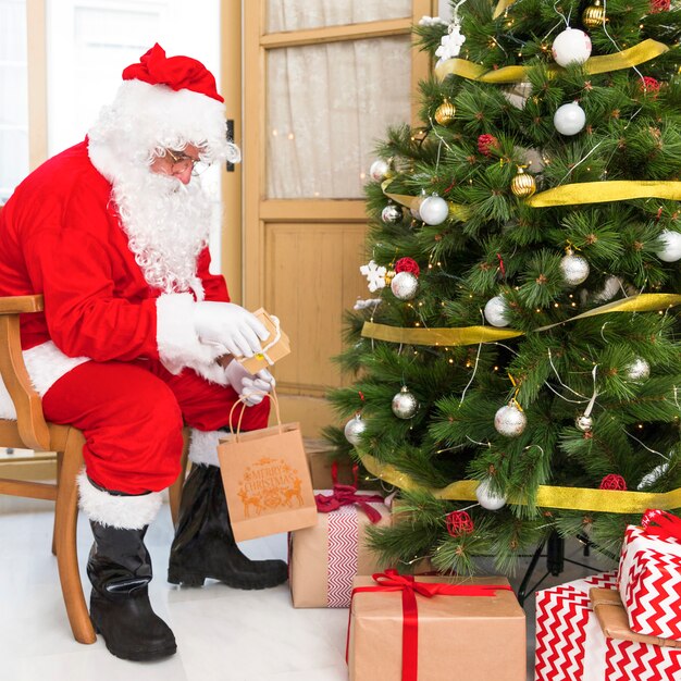 Santa Claus on chair putting gifts under tree