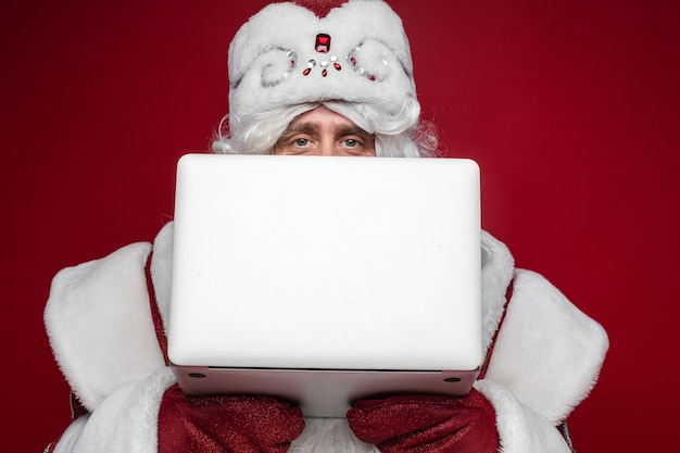 Free photo santa claus hiding behind laptop