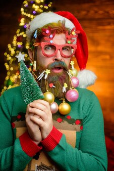 Санта-клаус держит елку в новогодней одежде канун нового года санта в доме санта-клаус с рождеством и