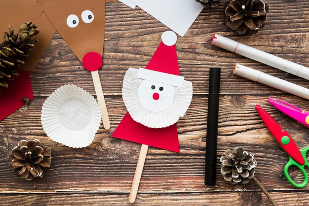 Santa claus and reindeer props with pinecones; felt-tip pen and scissor on wooden desk