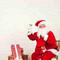 Free photo santa claus ringing bell sitting on chair