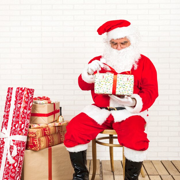 Free photo santa claus sitting and holding present in hands