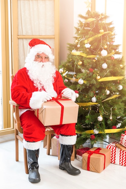 Babbo Natale seduto vicino albero di Natale con presente