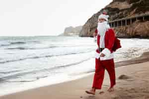 Foto gratuita babbo natale che cammina sulla vista laterale della spiaggia