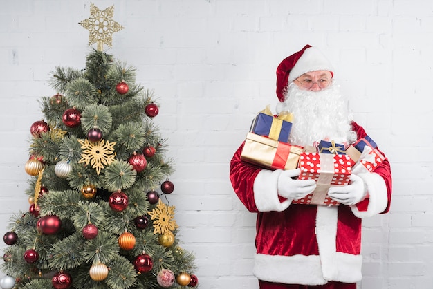 Santa Claus with gifts in hands near Christmas tree