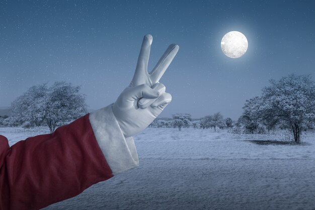 夜の満月の雪原で手のジェスチャーでサンタクロース。メリークリスマス