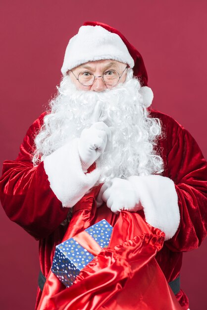 Santa Claus with sack of gifts showing secret gesture