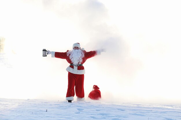 冬​の​野原​の​サンタ​。​フィールド​に​沿って​歩く​サンタ​の​魔法​の​霧​。​クリスマスイブ​の​サンタ​は​赤い​バッグ​で​子供たち​に​プレゼント​を​運んでいます