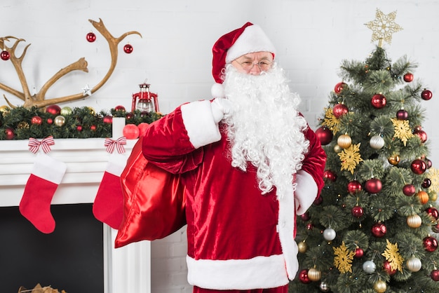 Санта с большим мешком подарков возле елки